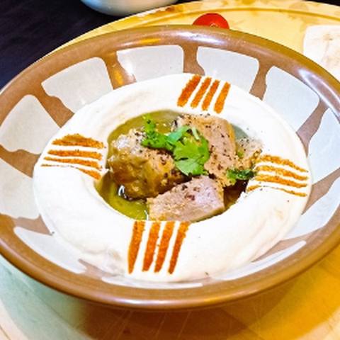 Abu Mubarak Authentic Chicken Hummus in a traditional clay bowl, featuring smooth, creamy hummus topped with tender pieces of spiced chicken, fresh coriander, and a drizzle of olive oil.
