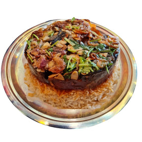 Abu Mubarak Lambshank Maqlubah for four people, featuring tender slow-cooked lamb shanks and golden fries on a grand bed of aromatic spiced basmati rice, garnished with lemon and fresh vegetables on a silver platter.
